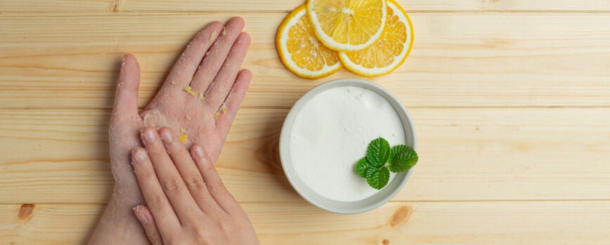Mulher jovem aplicando esfoliante de limão natural nas mãos contra a mesa de madeira