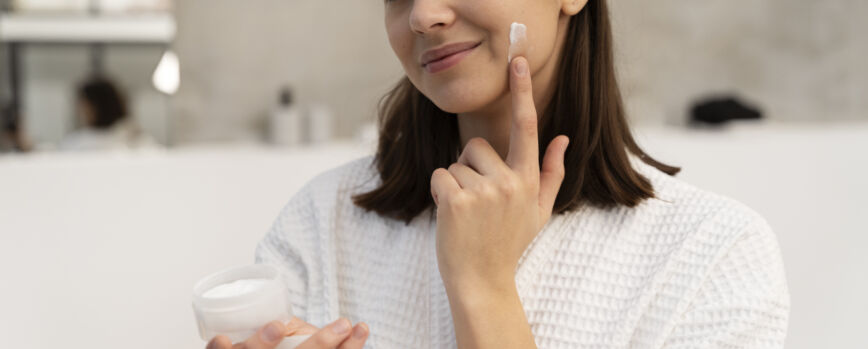 Mulher jovem aplicando creme hidratante no rosto antes de tomar um banho