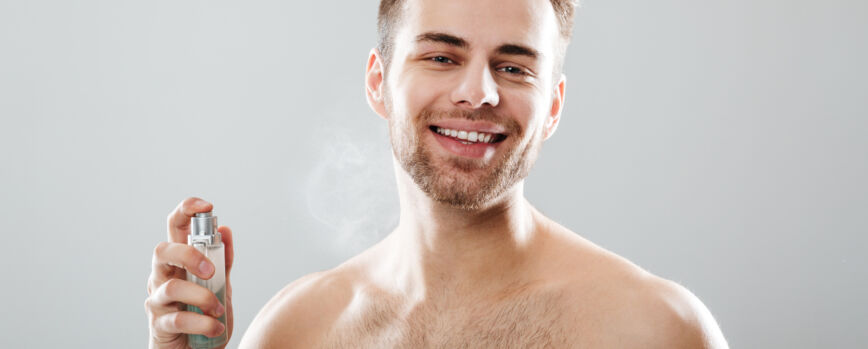 Retrato de um homem seminu sorridente borrifando perfume