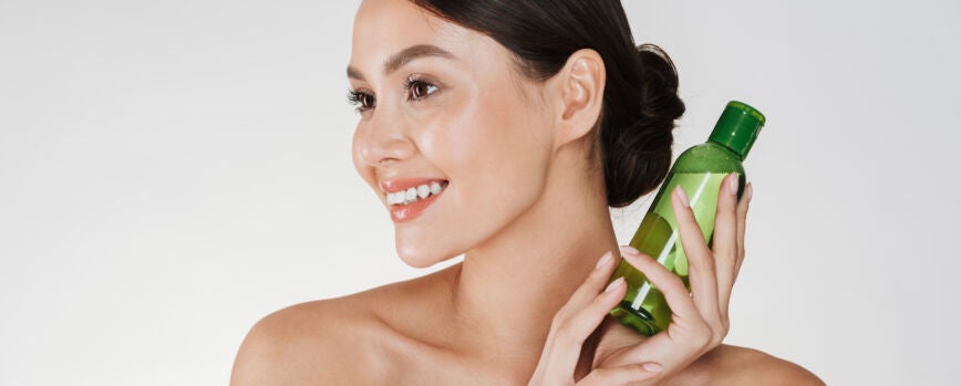 Retrato de beleza de mulher morena sorridente com pele suave e saudável com loção para remover maquiagem, isolado em branco