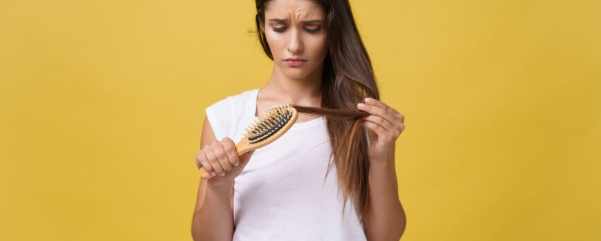 Mão de mulher segurando seu cabelo longo enquanto olha as pontas danificadas dos problemas de cuidado do cabelo