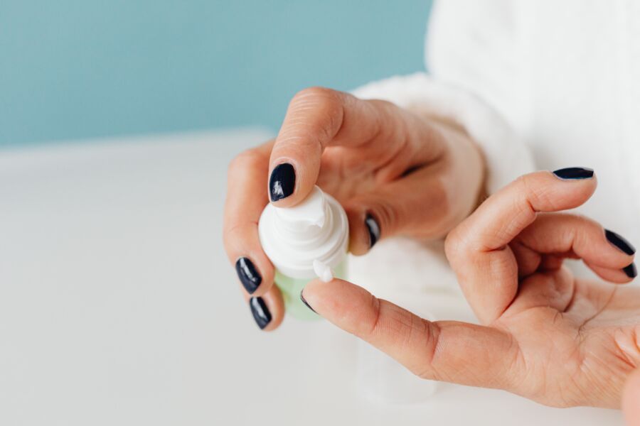 Fotografia detalhada das mãos aplicando creme para o cuidado da pele com um foco suave.
