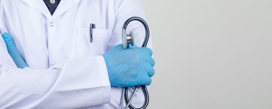 Médico cruzando os braços enquanto segura um estetoscópio em um jaleco branco