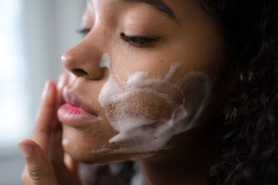 Uma mulher aplicando espuma para cuidados com a pele no rosto para uma rotina de limpeza suave.