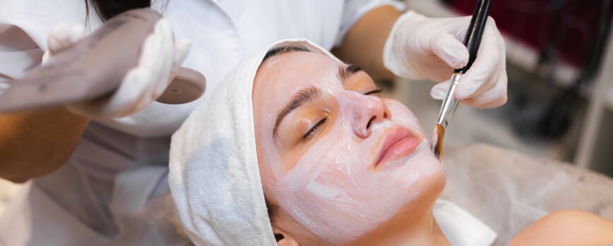 Esteticista com um pincel aplica uma máscara hidratante branca no rosto de um cliente jovem em um salão de beleza spa