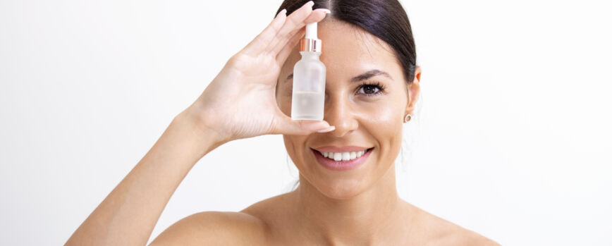 Mulher bonita jovem que recebe um tratamento especial para a pele. Linda garota aplicando sérum isolada sobre fundo branco. Pele suave sem rugas.