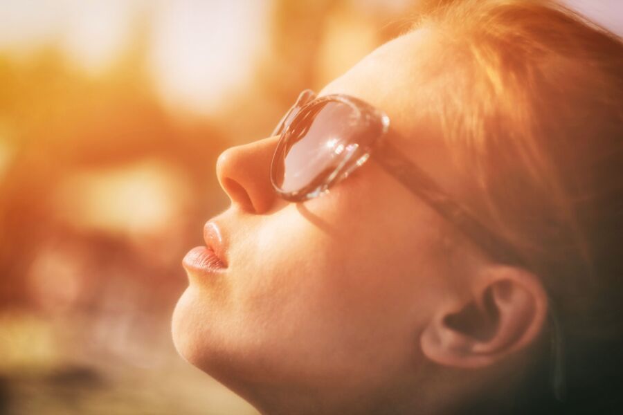 Retrato em primeiro plano de uma mulher com óculos de sol desfrutando da luz do sol e da relaxação ao ar livre.