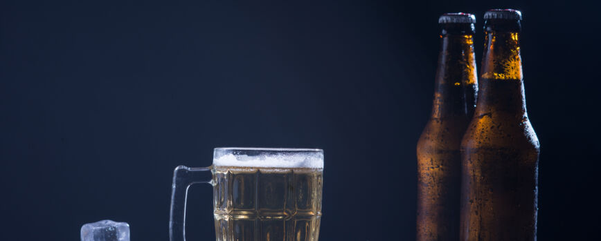 Garrafas de vidro de cerveja com vidro e gelo em fundo escuro