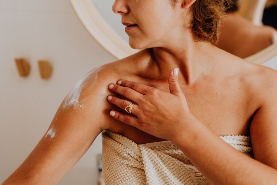 Uma mulher aplica loção corporal para o cuidado da pele, destacando as rotinas de autocuidado e beleza.