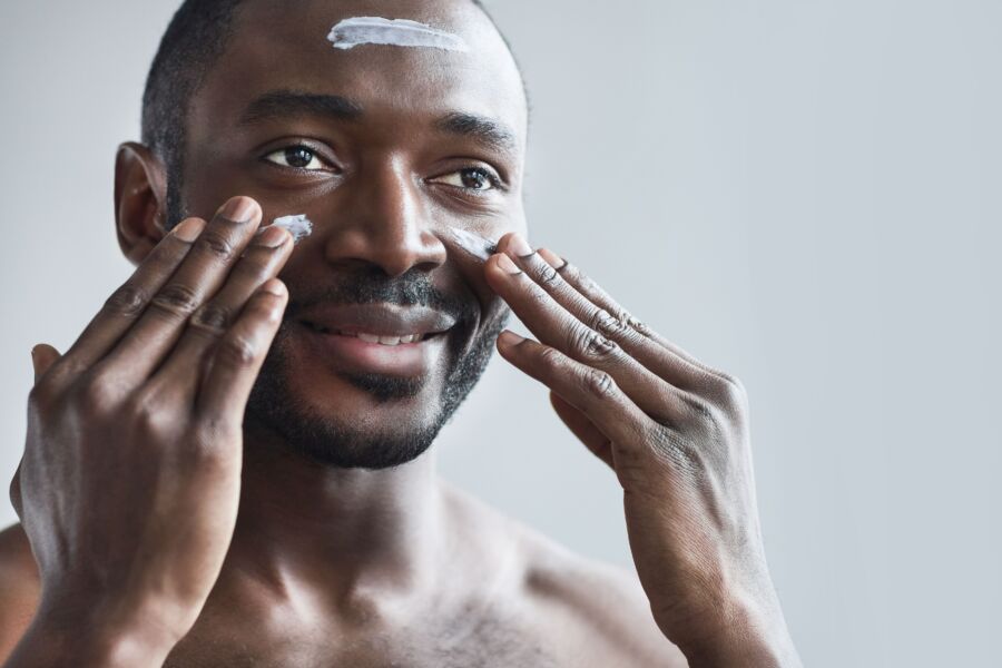 Homem sorridente aplicando creme facial como parte de sua rotina diária de cuidados com a pele para uma pele saudável.