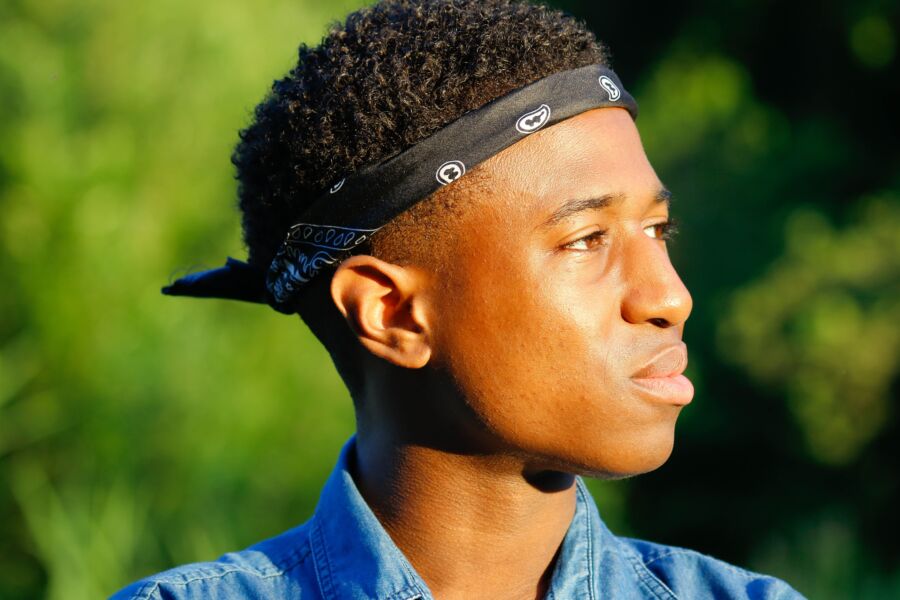 Retrato de um jovem com camisa jeans e lenço, olhando para longe, fotografado à luz natural do sol.