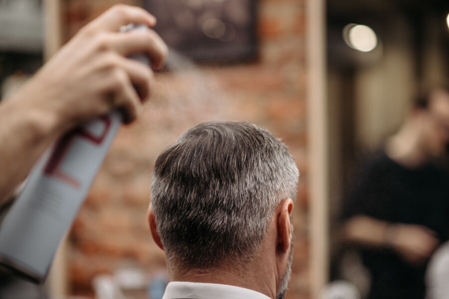 Um barbeiro profissional penteia o cabelo de um homem com spray em uma barbearia urbana.