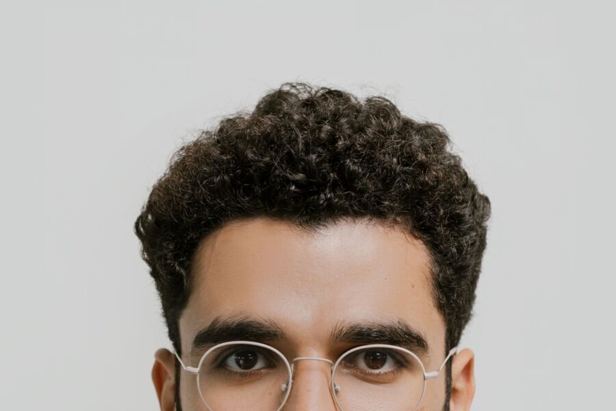 Retrato detalhado em close de um homem com cabelo cacheado e óculos.