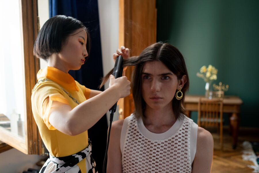 Um cabeleireiro penteando o cabelo de um cliente com uma chapinha em um salão contemporâneo.
