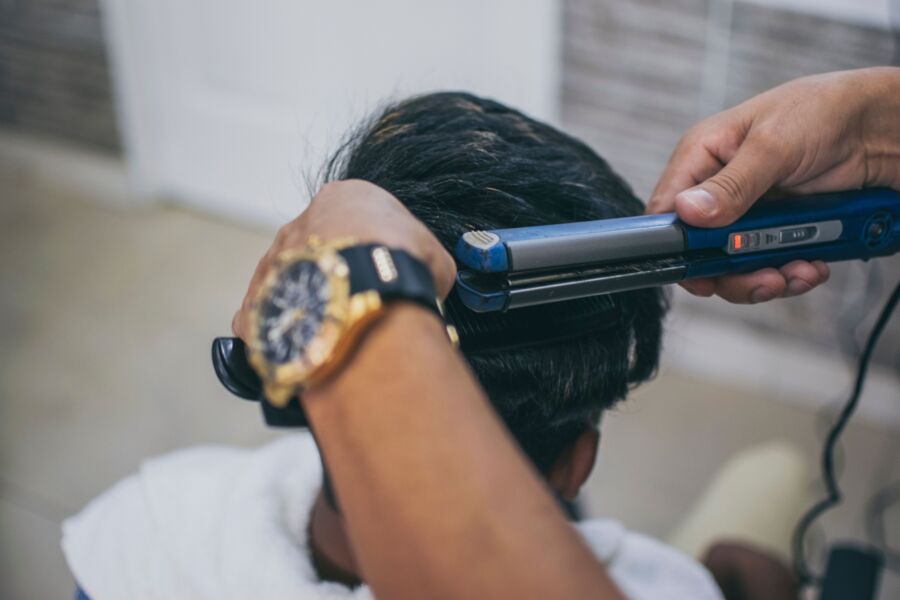 Close-up de um cabeleireiro penteando o cabelo de um cliente com uma chapinha em uma barbearia.