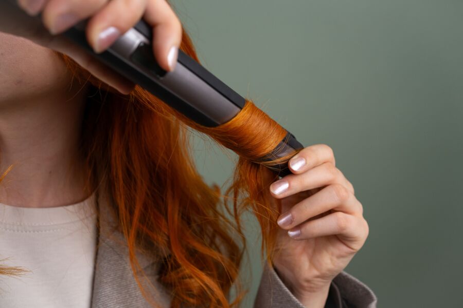 Close-up de uma mulher cacheando seu vibrante cabelo vermelho com um modelador.