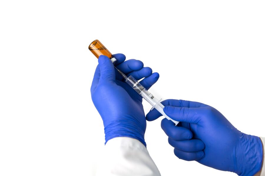 Médico irreconhecível em luvas protetoras azuis com frasco de seringa de preenchimento de fármaco com vacina contra fundo branco durante a pandemia de coronavírus